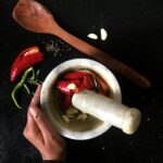 Spicy ingredients including chili peppers, garlic, and spices in a mortar for food preparation.